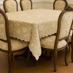May include: A dining set featuring a square table covered with a beige floral patterned tablecloth. Six matching chairs with ornate wooden frames and beige floral upholstery surround the table. The chairs have curved backs and carved details.