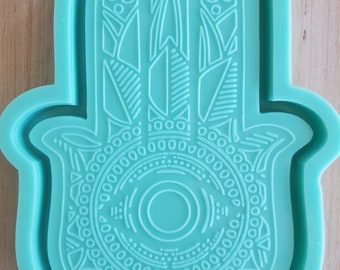 Puede incluir: Un molde de silicona azul turquesa con forma de mano de hamsa con intrincados diseños geométricos. El molde está diseñado para crear artesanías de resina.