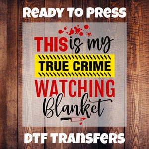 May include: A DTF transfer design with the text "READY TO PRESS". The design features the phrases "THIS is my TRUE CRIME WATCHING Blanket" in a mix of fonts and colours, with a blood splatter and knife graphic. The background is a wood grain pattern.