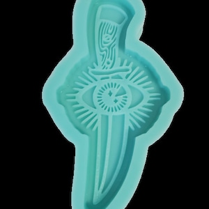 Könnte beinhalten: Eine türkisfarbene Silikonform zum Herstellen von Kunsthandwerk aus Harz. Die Form zeigt ein Dolch mit einem Auge und einem Stern.