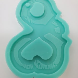 May include: A teal blue silicone mold shaped like a cartoon character with a large head and a small body. The mold has a detailed design with a round eye and a small mouth.