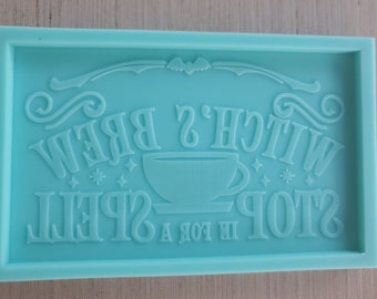 May include: A teal blue silicone mold with the text "Witch's Brew Stop in for a Spell" in a decorative font. The mold also features a small coffee cup graphic.