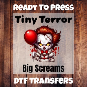 May include: A DTF transfer featuring a cartoon clown with red hair, holding a red balloon. The clown has white face paint, stitched scars, and a red bow tie. The text "READY TO PRESS", "Tiny Terror", "Big Screams", and "DTF TRANSFERS" is included.