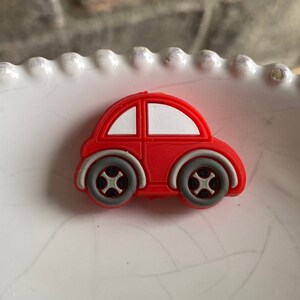 May include: A red toy car with white windows and gray wheels. The car is made of rubber and has a simple design.
