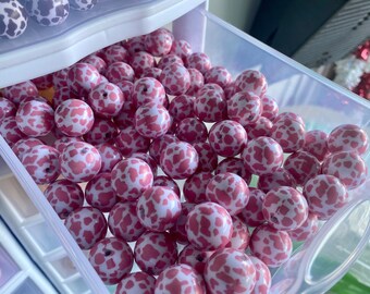 May include: A close-up of a drawer filled with pink and white cow print beads. The beads are round and have a glossy finish.