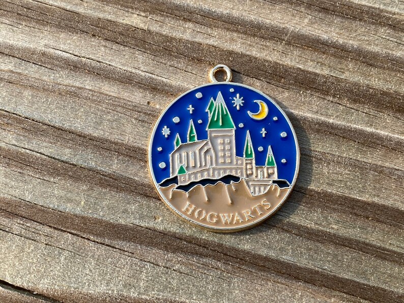 Puede incluir: Un pin de esmalte azul y dorado con una ilustraci&oacute;n detallada del castillo de Hogwarts con una luna creciente y estrellas. El pin dice "HOGWARTS" en la parte inferior.
