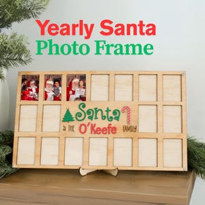 Può includere: Una cornice portafoto rettangolare in legno chiaro con quindici scomparti per immagini. Il centro presenta un'icona di albero di Natale verde, il testo Santa, un'icona di bastoncino di zucchero e il testo The O'Keefe Family in rosso.