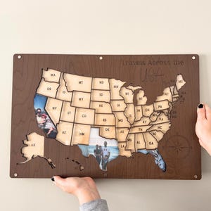 Może przedstawiać: Drewniana mapa USA z wycięciami poszczeg&oacute;lnych stan&oacute;w. Mapa ma zdjęcia wstawione w niekt&oacute;rych stanach. Tekst "Travels Across the USA" znajduje się nad mapą. Mapa jest trzymana przez dwie ręce.
