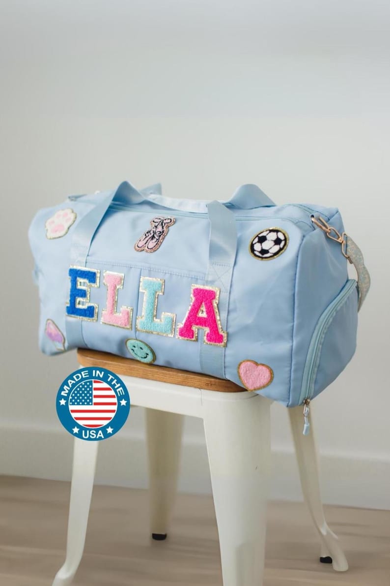 Light blue personalized duffel bag with chenille varsity letters spelling ELLA and fun patches (soccer ball, heart, smiley), custom travel bag for girls, teens, dance, cheer, gymnastics, or sleepovers.