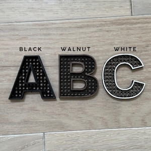 K&ouml;nnte beinhalten: Drei Holzbuchstaben, A, B und C, in Schwarz, Walnuss und Wei&szlig;. Die Buchstaben werden auf einer hellen Holzoberfl&auml;che angezeigt. Das Wort "BLACK" steht &uuml;ber dem Buchstaben A, "WALNUT" &uuml;ber B und "WHITE" &uuml;ber C.