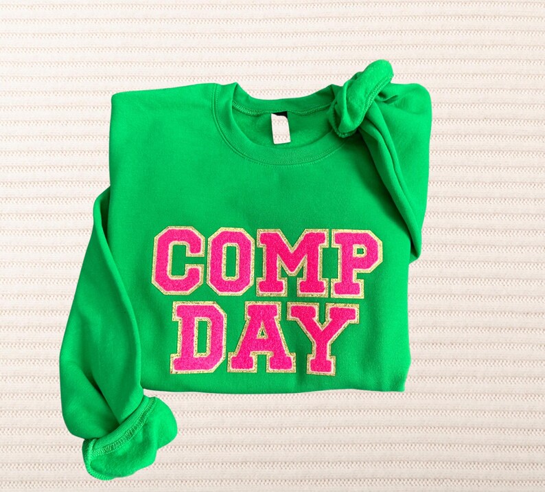May include: Green sweatshirt with the words "COMP DAY" in pink glitter letters.