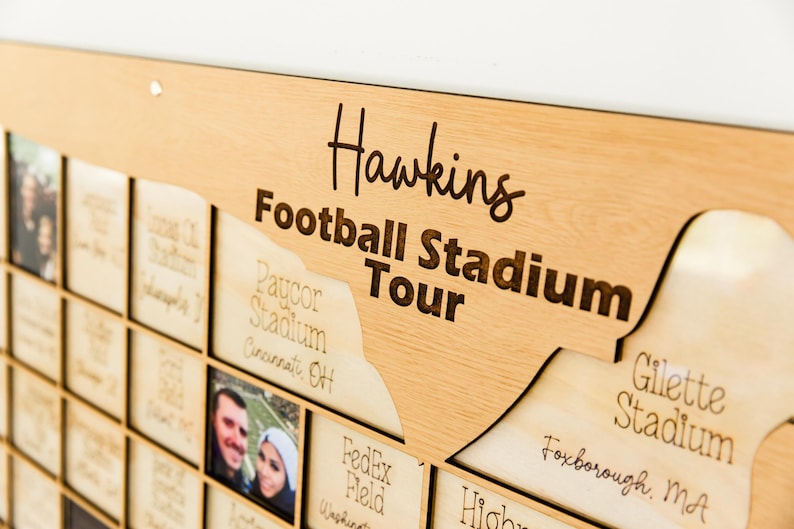 May include: A wooden wall art piece with the words "Hawkins Football Stadium Tour" engraved in a stylish font. The artwork features a map-like design with cutouts for photos and stadium names, including "Gillette Stadium" and "Paycor Stadium."