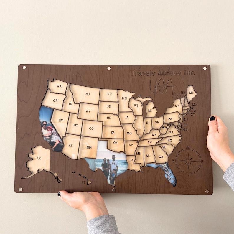Może przedstawiać: Drewniana mapa USA z wycięciami poszczeg&oacute;lnych stan&oacute;w. Mapa ma zdjęcia wstawione w niekt&oacute;rych stanach. Tekst "Travels Across the USA" znajduje się nad mapą. Mapa jest trzymana przez dwie ręce.