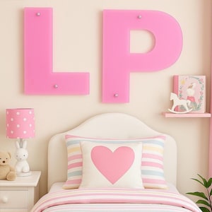 May include: Pink and white striped bedding with a pink heart pillow and a white lamp with pink polka dots. The wall behind the bed has large pink letters that spell "LP".