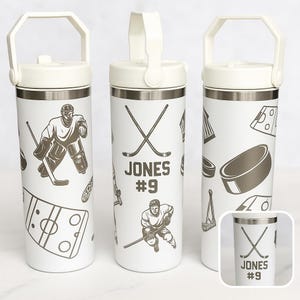 May include: White insulated water bottle with a handle, featuring hockey-themed graphics. The design includes hockey players, crossed hockey sticks, pucks, and the name "JONES #9". The bottle has a white lid and a silver band.