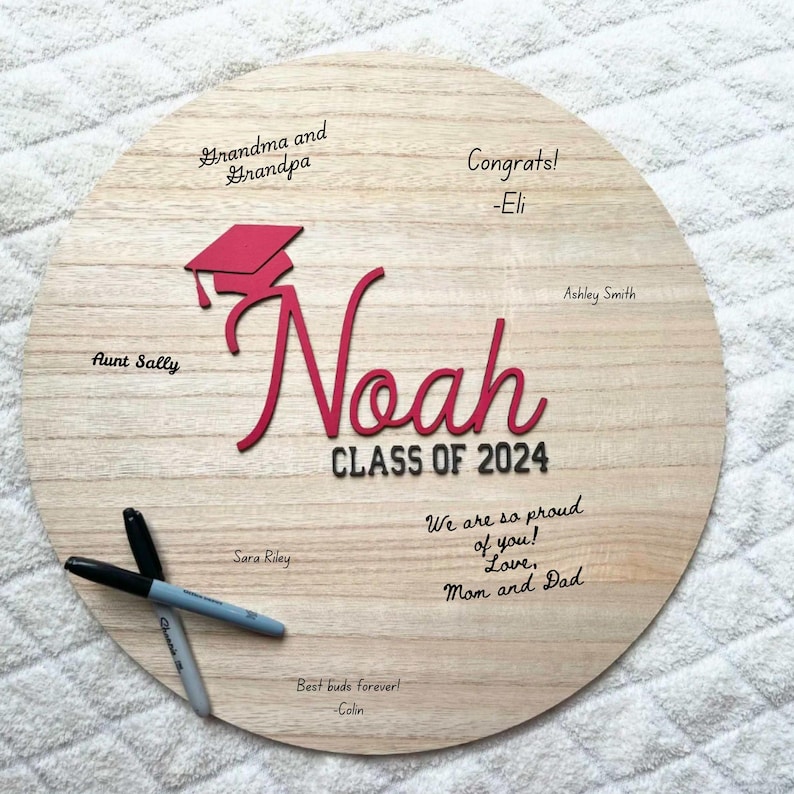 May include: A round wooden sign with the name "Noah" in red lettering and a graduation cap. The sign also includes the text "Class of 2024" and messages from family and friends.