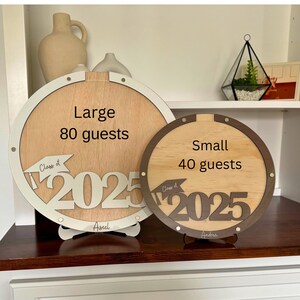 May include: Two wooden graduation guest book alternatives. The large one is white with the text "Large 80 guests" and "Class of 2025". The small one is brown with the text "Small 40 guests" and "Class of 2025".