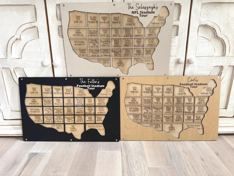 May include: Three wooden stadium tour maps in the shape of the United States. The top map is beige with the text "The Salasznyk's NFL Stadium Tour". The other two maps are black and light brown with the text "The Fuller's Football Stadium Tour" and "Carl's Football Stadium Tour".