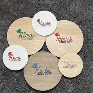 May include: Six round wooden signs with the names Alexis, Kierah, Anna, Karley, Patrick, and Carsun, each with the text "Class of 2024" and a graduation cap graphic.