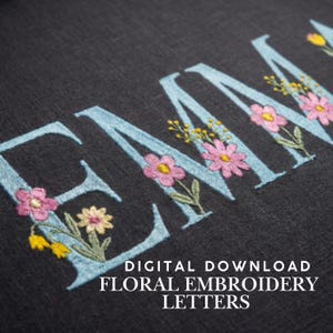 May include: Close-up of embroidered letters spelling "EMMA" in light blue, adorned with pink and yellow floral designs on a dark gray fabric. The text "DIGITAL DOWNLOAD FLORAL EMBROIDERY LETTERS" is at the bottom.