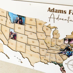 Może przedstawiać: Drewniana mapa Stan&oacute;w Zjednoczonych z konturami stan&oacute;w i wstawionymi zdjęciami. Mapa jest oznaczona jako "Adams Family Adventures" czcionką odręczną. R&oacute;ża wiatr&oacute;w znajduje się w prawym dolnym rogu.