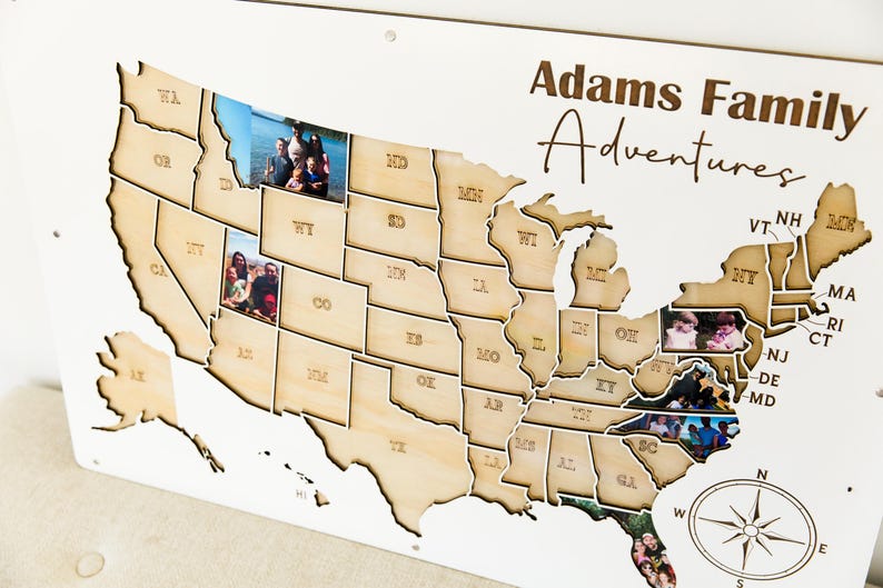 Może przedstawiać: Drewniana mapa Stan&oacute;w Zjednoczonych z konturami stan&oacute;w i wstawionymi zdjęciami. Mapa jest oznaczona jako "Adams Family Adventures" czcionką odręczną. R&oacute;ża wiatr&oacute;w znajduje się w prawym dolnym rogu.