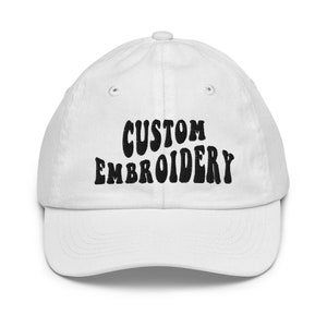 Peut inclure: Casquette de baseball blanche avec un texte brodé en noir qui dit "CUSTOM EMBROIDERY" dans une police rétro.