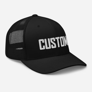 May include: Black trucker hat with a white embroidered "CUSTOM" text on the front.
