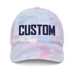 May include: A blue and pink tie-dye baseball cap with the word "CUSTOM" embroidered in navy blue.