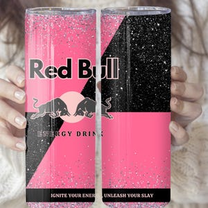 May include: A pink and black tumbler featuring the Red Bull logo with two bulls and the words "ENERGY DRINK". The tumbler has a glittery finish and the text "IGNITE YOUR ENERGY" and "UNLEASH YOUR SLAY".
