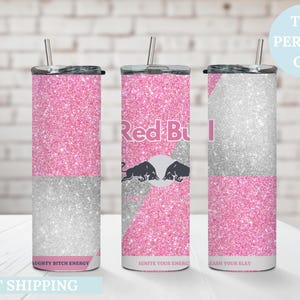 May include: Three glitter-covered tumblers with straws. The tumblers are pink and silver, with the Red Bull logo on one. Text on the tumblers reads "NAUGHTY BITCH ENERGY", "IGNITE YOUR ENERGY", and "UNLEASH YOUR SLAY".