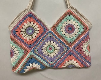 Può includere: Una borsa a tracolla in crochet con un cinturino bianco e un design patchwork colorato. La borsa è realizzata con quadrati con fiori di diversi colori al centro.