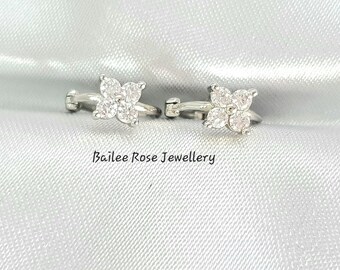 May include: A pair of silver earrings with a four-leaf clover design featuring clear cubic zirconia stones. The earrings are clip-on style.