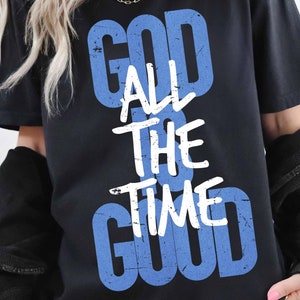 以下が含まれることがあります： 「God All The Time Good」と書いてある、青と白のグラフィックがプリントされた黒いTシャツです。