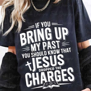May include: Black t-shirt with white text that reads "If you bring up my past you should know that Jesus dropped the charges". A white bible is pictured below the text.