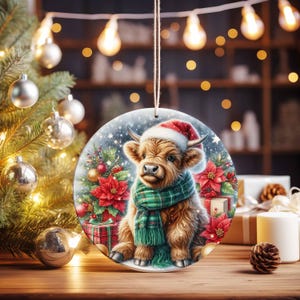May include: Round Christmas ornament featuring a Highland cow wearing a Santa hat and green plaid scarf. The ornament has a festive design with a Christmas tree, poinsettias, and wrapped gifts. It is hanging from a string.