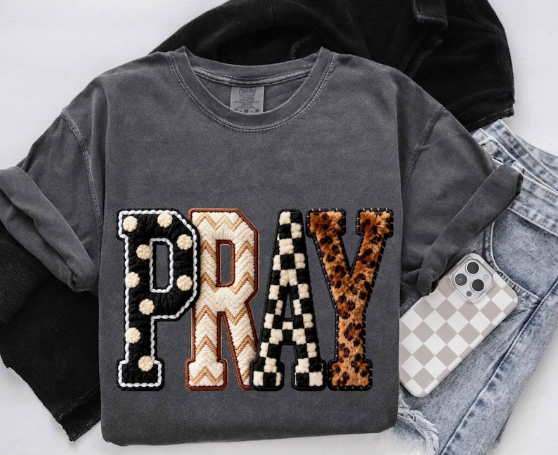 Op de afbeelding: Donkergrijze sweatshirt met het woord "PRAY" in een patchwork-ontwerp. De letter "P" is zwart met witte stippen, "R" is cr&egrave;me met een bruin zigzagpatroon, "A" is zwart-wit geblokt en "Y" is luipaardprint.