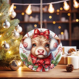 May include: A round Christmas ornament featuring a Highland cow with a red bow, earmuffs, and scarf. The ornament is decorated with candy canes, snowflakes, and greenery. A festive holiday decoration.