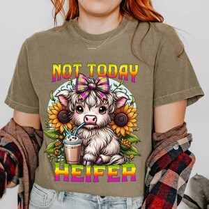 May include: A brown t-shirt with a cartoon cow wearing a pink and yellow bow and drinking a milkshake. The text "Not Today Heifer" is printed on the shirt.