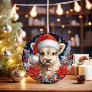 May include: A round Christmas ornament featuring a Highland cow wearing a Santa hat. The ornament has a dark blue background with red poinsettias, pinecones, and snowflakes. A small gold bell hangs from the cow's neck. The ornament is hanging from a string.