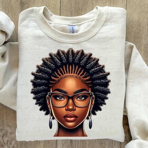 May include: Cream-colored sweatshirt featuring a detailed illustration of a Black woman with dark skin, wearing black-framed glasses and earrings. Her hair is styled in intricate braids. The design is centered on the front of the long-sleeved top.