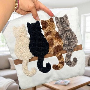 Könnte beinhalten: Ein weißes Kissen mit vier strukturierten Katzen-Silhouetten in Creme, Schwarz, Braun und Grau, die auf einem braunen Holzbalken sitzen. Die Schwänze der Katzen sind eingerollt. Ein charmantes, handgefertigtes Dekorationsstück.