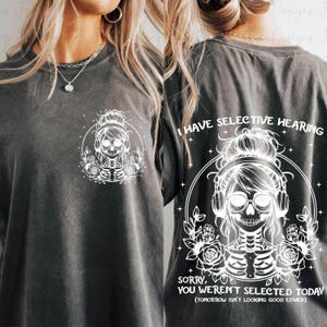 May include: A black t-shirt with a white graphic of a skeleton wearing headphones and a bun. The text "I have selective hearing" is above the graphic and the text "Sorry, you weren't selected today (tomorrow isn't looking good either)" is below the graphic.