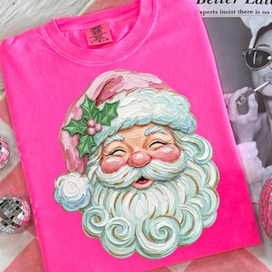 Könnte beinhalten: Ein leuchtend pinkfarbenes Comfort Colors Sweatshirt mit einer detaillierten Illustration des Weihnachtsmanns. Der Weihnachtsmann hat ein rosiges Gesicht, einen weißen Bart und einen rosa-blauen Hut. Das Design umfasst Stechpalmenblätter und Beeren. Das Shirt ist Größe L.