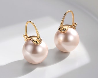 May include: A pair of gold hoop earrings with a single large pearl on each hoop. The pearls are a light pink color.