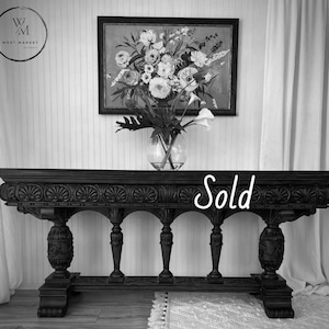 May include: A dark wood console table with ornate carvings and arched supports. A framed floral painting and a glass vase with flowers are displayed above the table. The word "Sold" is written across the table.