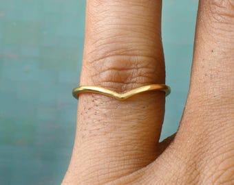 May include: A gold-coloured chevron ring. The ring has a simple band with a V-shaped design. The ring is worn on a finger.