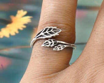 May include: A silver-colored ring featuring a leaf design. The ring wraps around the finger with two detailed leaf motifs. The leaves have intricate vein patterns, creating a nature-inspired accessory.