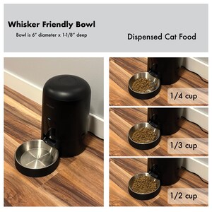 Op de afbeelding: Zwarte automatische kattenvoerdispenser met een roestvrijstalen kom. De tekst luidt "Whisker Friendly Bowl" en "Dispensed Cat Food". De kom heeft een diameter van 15,2 cm en is 2,9 cm diep. De afbeelding toont porties van 1/4, 1/3 en 1/2 kopje.