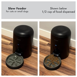 Op de afbeelding: Zwarte slowfeeder voor katten of kleine honden. De feeder geeft 1/2 kopje voer af in een grijze kom met een doolhofontwerp. De feeder is cilindrisch met een afgeronde bovenkant en een klein blauw lampje.